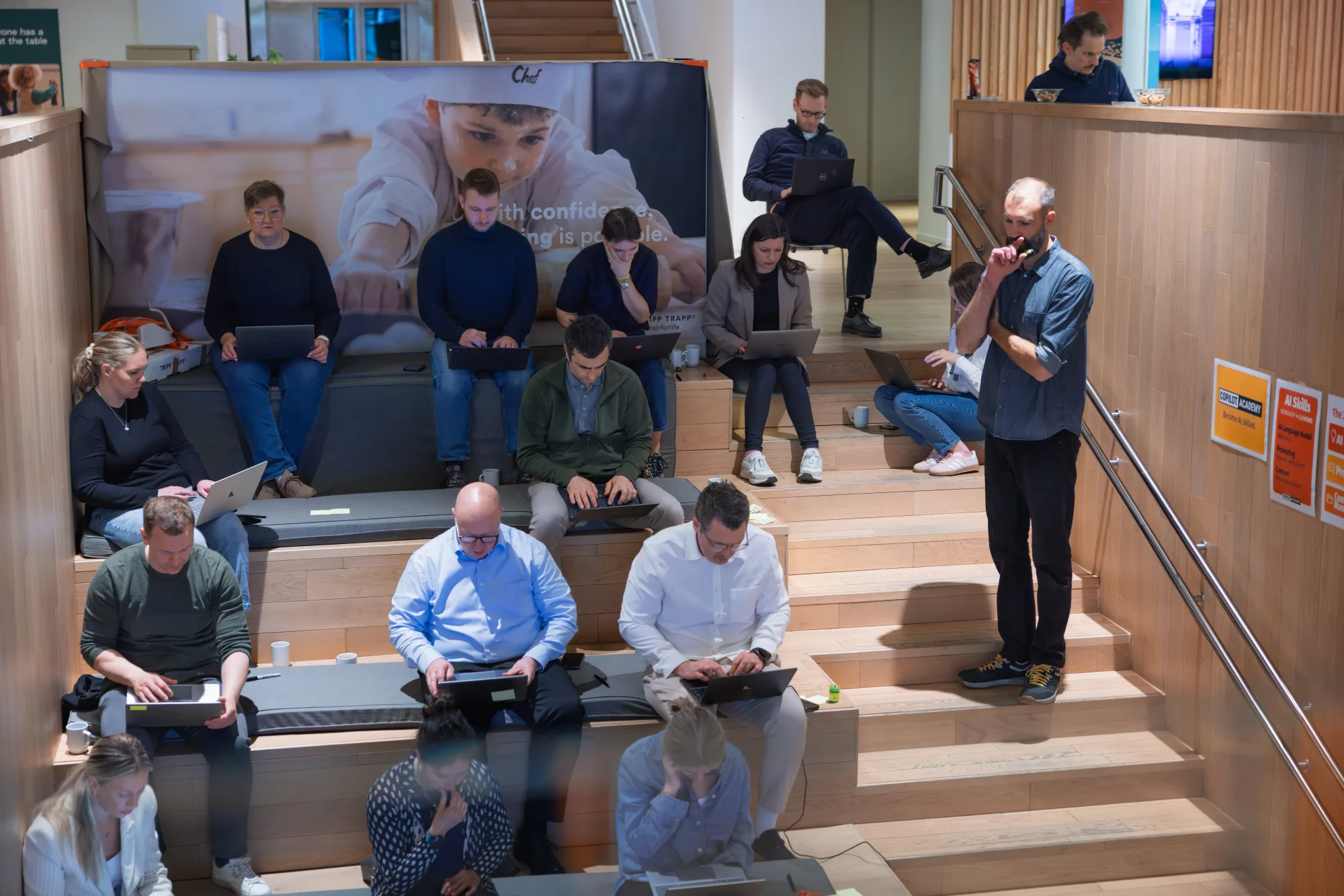 Trainer loopt rond tijdens een werksessie, deelnemers werken op laptops