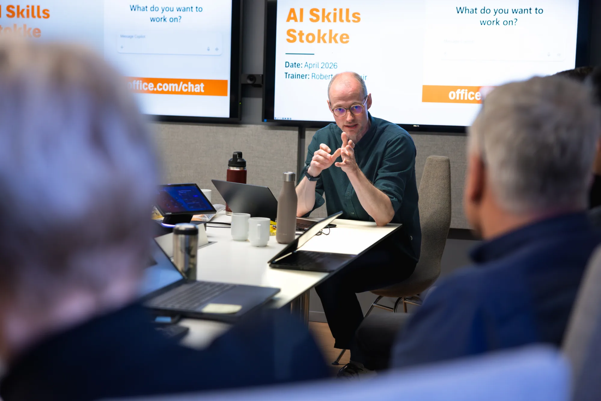 Robert opent een AI Skills sessie aan een conferentietafel met twee schermen op de achtergrond